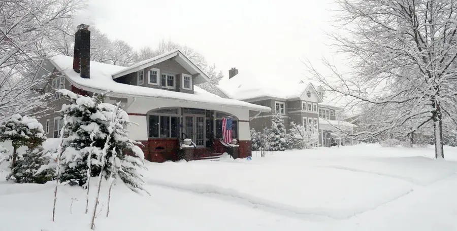 A snow-covered bungalow and yard after a winter storm, the season that drives frozen pipe and ice dam losses around Concord, NH