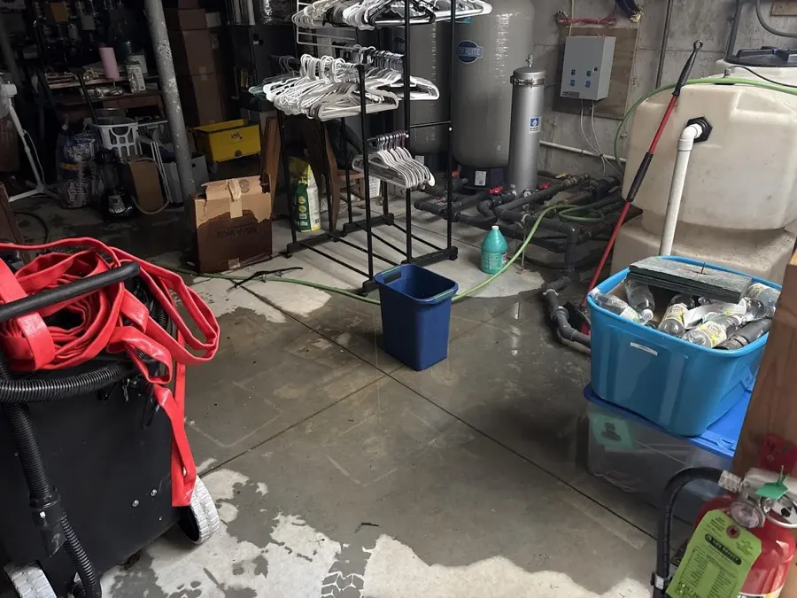 A wet concrete floor in a basement utility room with a storage tank and bins, basement water damage