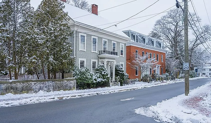 Older clapboard and brick houses along a snowy New England street in winter
