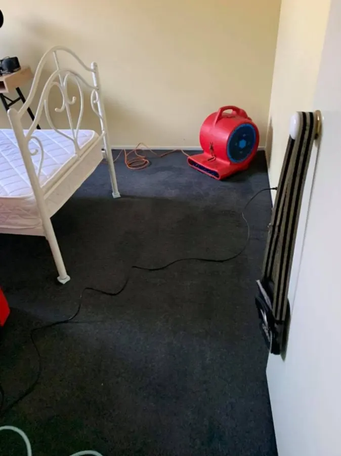 Bedroom in a Hooksett home with the carpet pulled up and a red air mover drying the floor during water damage restoration