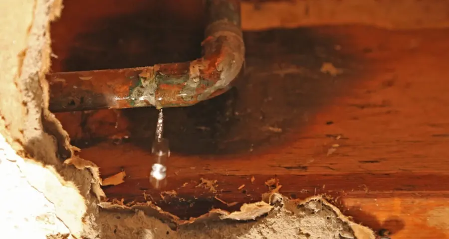 A corroded pipe dripping water inside an opened wall cavity, burst pipe water damage in Concord, NH