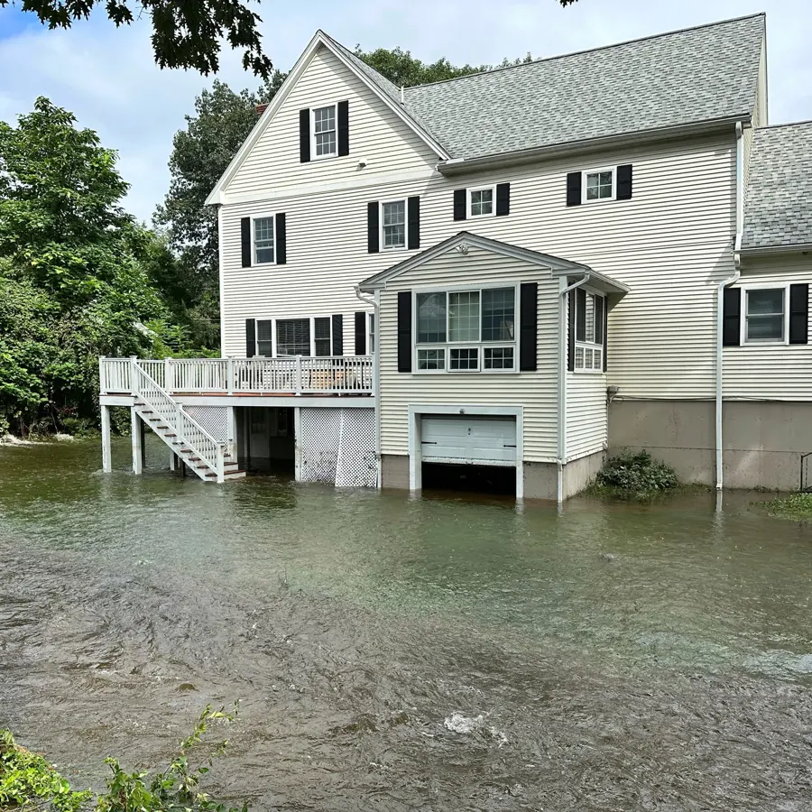 Floodwater surrounding a white two-story house and its garage door, flood water cleanup in Concord, NH