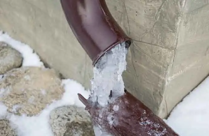 A split pipe packed with ice against a snowy foundation wall, frozen pipe water damage in Concord, NH