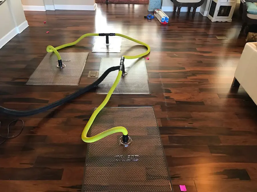 Drying mats with yellow vacuum hoses set on a wet hardwood floor, hardwood floor drying in Concord, NH
