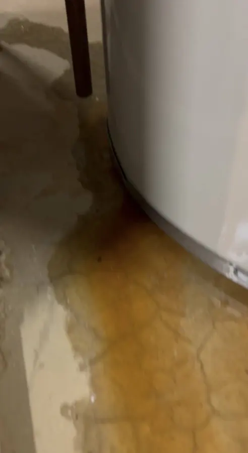 Rusty water pooling around the base of a water heater tank, water heater leak cleanup in Concord, NH